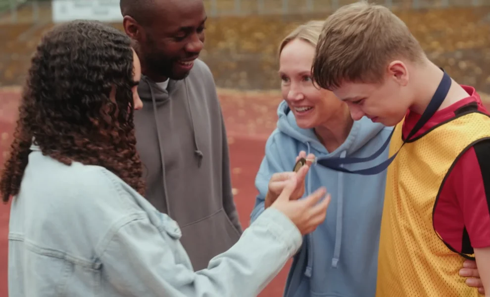 Four people standing outside and talking to one another. The boy is wearing a medal.