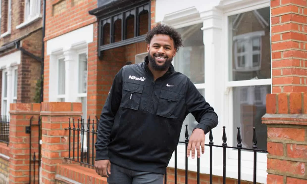 Camden foster carer Trevor Elliott standing outside of a home, leaning against a metal railing. He is smiling at the camera.