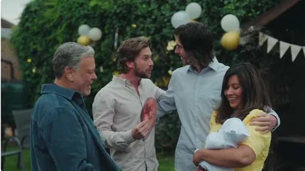 Four people standing together outside and talking at a party in a garden. One person is smiling and holding a baby.