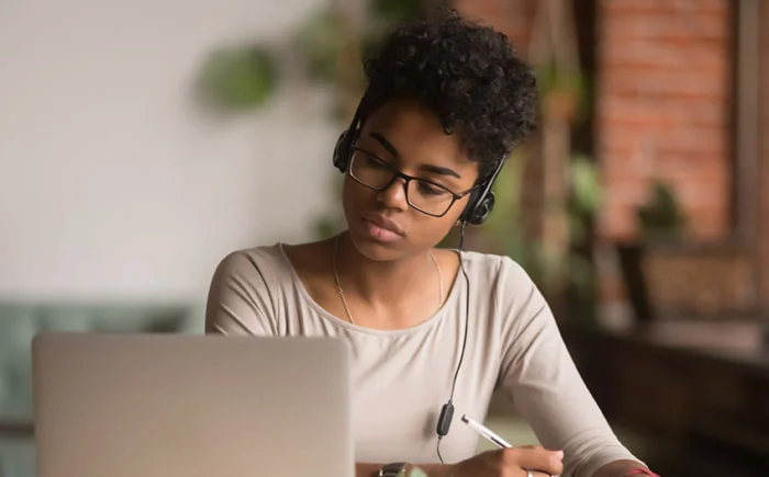 A woman wearing headphones looking at a laptop screen.