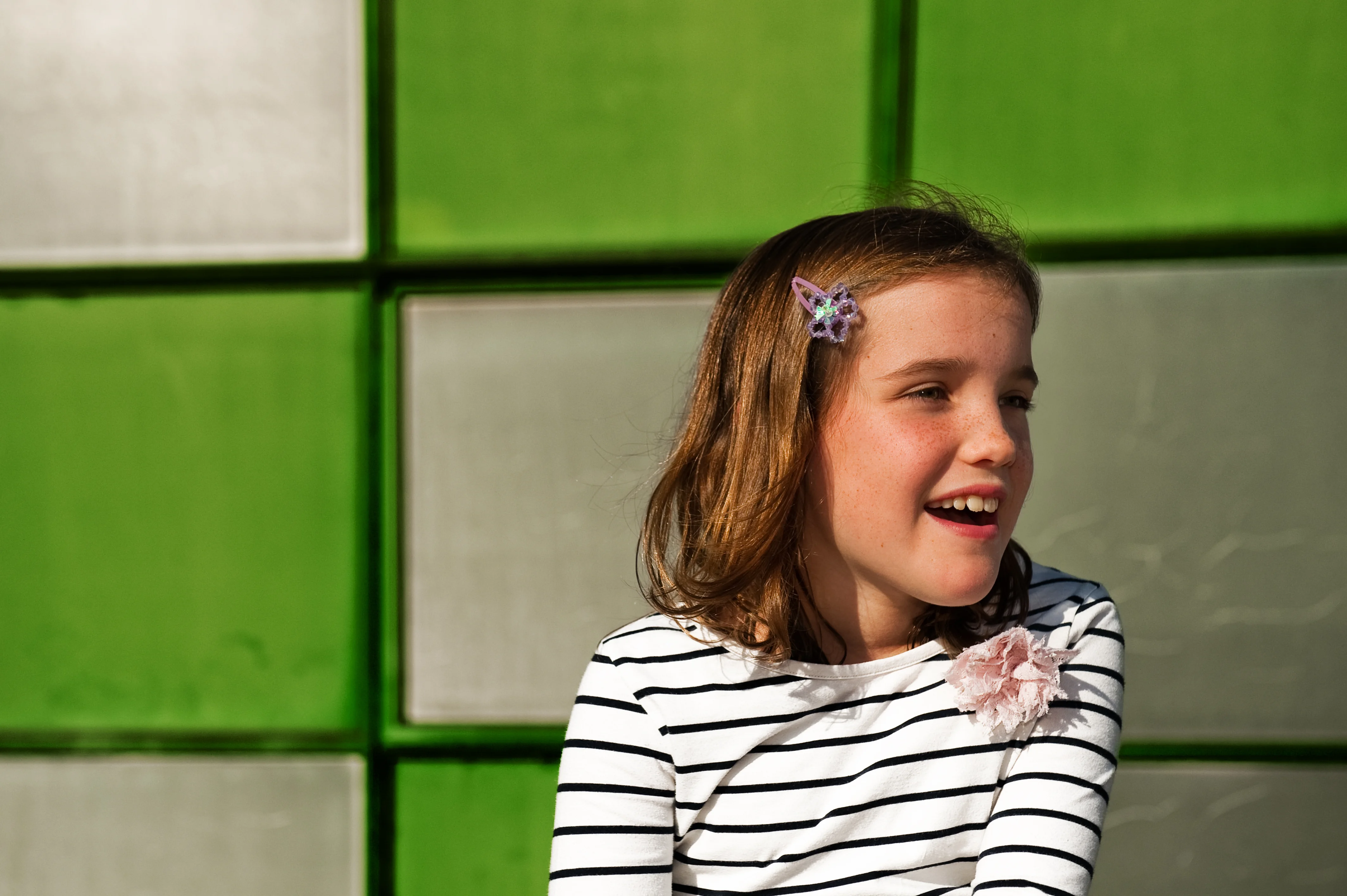 A young girl in a black and white striped top is smiling, facing away from the camera.